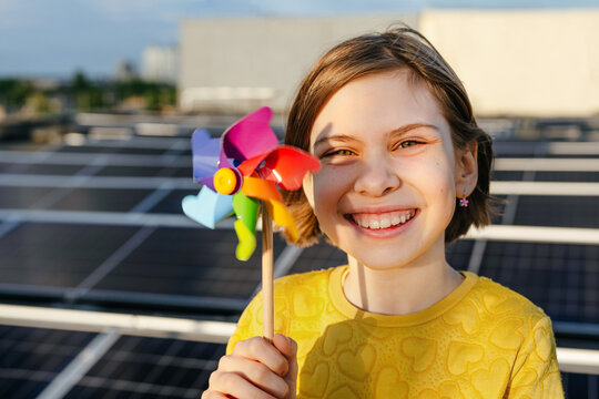 Smiling girl holds a colorful windmill toy near a solar panel