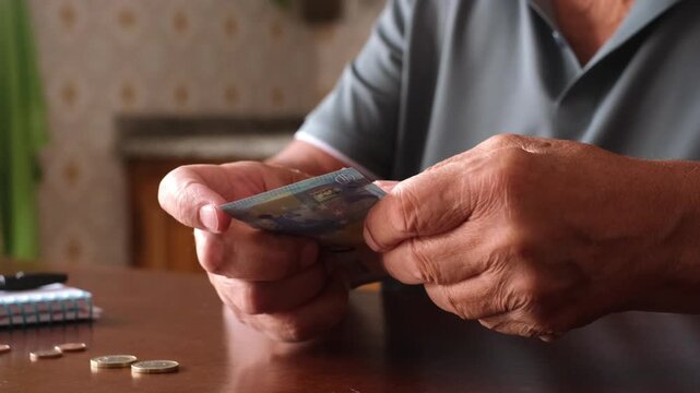 Close up of an elderly man's hands counting euro banknotes and coins on a wooden table, representing retirement savings, pension planning, and financial management in old age