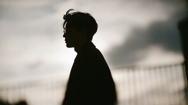 Growth mindset silhouette of a young man with glasses looking forward against a bright blurry sky and railing