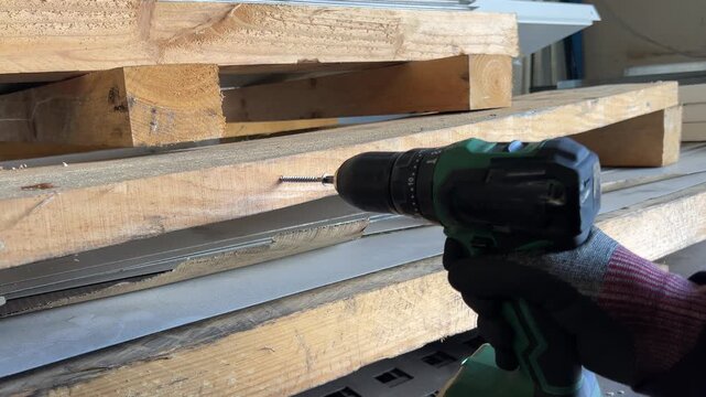 Worker using cordless screwdriver to drive screw into wooden pallet