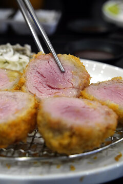Tender and juicy pink medium rare pork tenderloin tonkatsu held with chopsticks close up