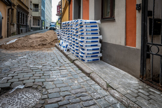 Sand Pile Dominates a Street Worksite Beside Stacked KNAUF Construction Material Bags