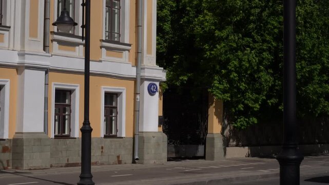 Historic pale yellow townhouse facade with lampposts and gated entrance on sunlit city street, with building, facade, townhouse, stucco detail, showing molding, window, stone, plinth context