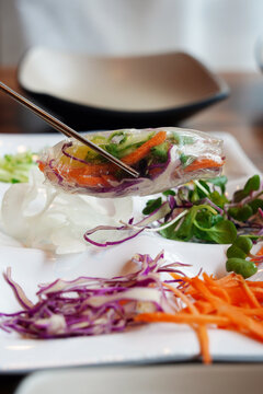 Fresh vietnamese spring roll wrapped in rice paper held with chopsticks over a salad plate
