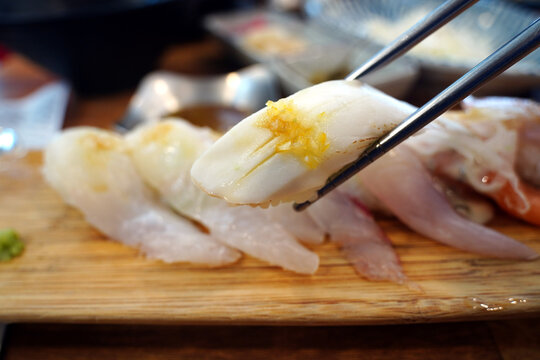 Fresh white fish sushi held with chopsticks over a wooden platter close up