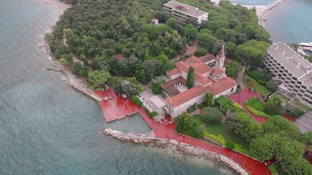 Aerial view of the Sveti Andrija island monastery surrounded by lush pine forests, red-tiled roofs, and the Adriatic Sea in Rovinj, Istria County, Croatia.