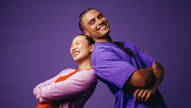 In a smiling studio portrait, friends stand back to back with youthful confidence