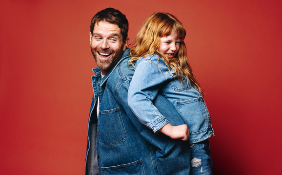 Playful moment showing a father and daughter smiling back to back in the studio