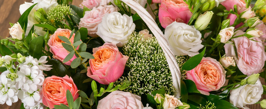 Beautiful bouquet of bright flowers in basket. Basket with roses.  Fowers over wooden background.