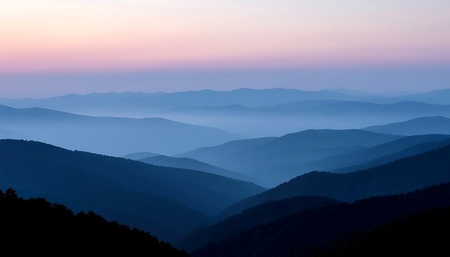 Misty mountain layers at sunrise with soft pastel sky and blue fog across scenic ridge hills