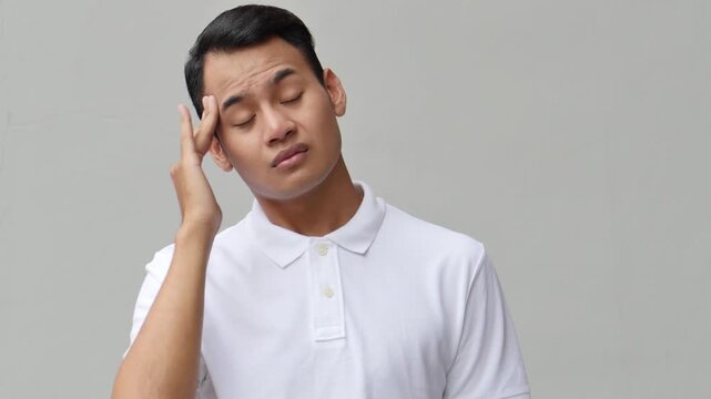 Southeast Asian young man touching head in pain from one sided headache