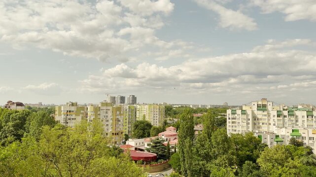 Modern apartment buildings stand surrounded by lush green trees in Simferopol, Crimea. A vast cloudy sky spreads above, bringing a peaceful feeling of calm home and hopeful warmth.