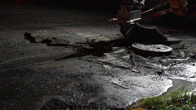 Close-up stock video footage of a heavy industrial excavator hydraulic breaker hammer aggressively breaking up road asphalt on a construction site.
