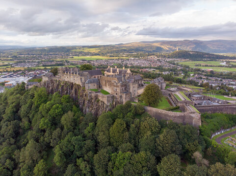 Aerial view of Stirling Castle perched on a rocky crag overlooking the city with lush trees and rolling hills in the background in Stirling, Scotland, United Kingdom.