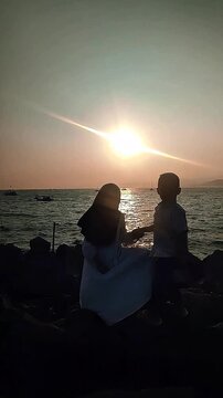 Silhouette of Romantic Muslim Couple Holding Hands on Rocky Beach During Sunset Golden Hour