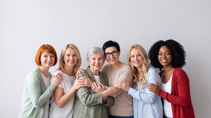 Obraz premium Group of diverse women of various ages standing together, smiling and embracing each other against a neutral background