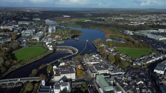 Aerial drone view of Limerick city showing the river winding through the urban area, with bridges, buildings, roads, green spaces, and surrounding countryside in Ireland.