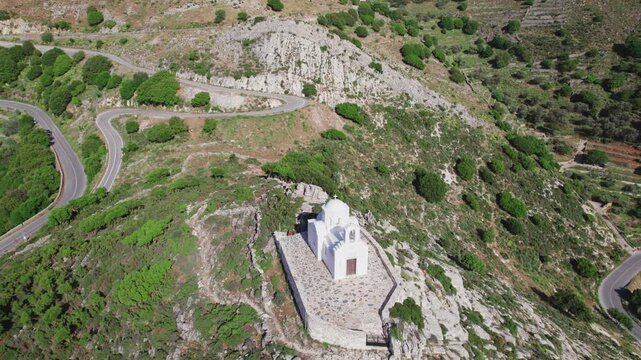 Traditional Greek Orthodox chapel perched on Naxos summit. Whitewashed Cycladic bell tower and dome amidst serene Aegean spiritual heritage by aerial drone 4k