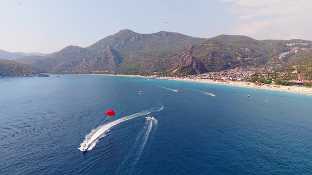 Drone flying over Parasail in &Ouml;l&uuml;deniz beach Turkey with mountains in the background