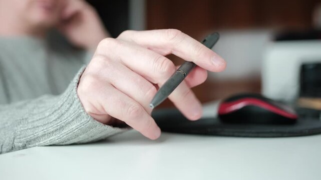 Person fidgeting with a pen while sitting at a desk