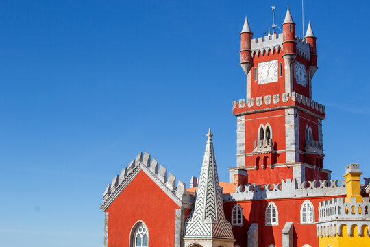 Sintra, Portugal - 18 August 2017: View of Pena Palace with its vibrant red and yellow facade, ornate clock tower, and intricate architectural details set against a clear blue sky.
