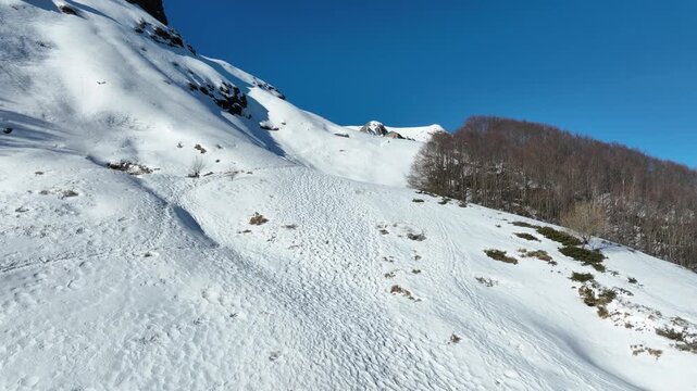 Aerial view of hikers trekking on the snow-covered slopes of Pania della Croce under a clear blue sky in Stazzema, Tuscany, Italy.