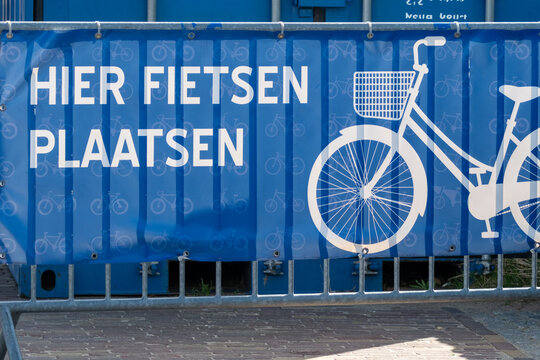 Sign displays bike parking information in a city area during daytime near a fence