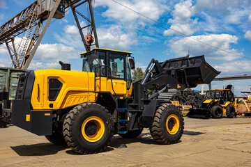 Fototapeta premium Large Yellow Wheel Loader with Raised Bucket at Industrial Yard