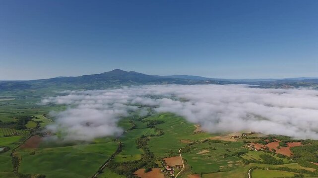 Aerial view of rolling green hills and low-lying clouds over the landscape of Pienza, Tuscany, Italy.