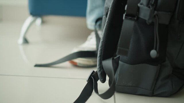 Close up of black backpack resting on floor with white sneakers and blue jeans visible in background. scene shows consistent soft lighting focusing solely on texture details like zippers