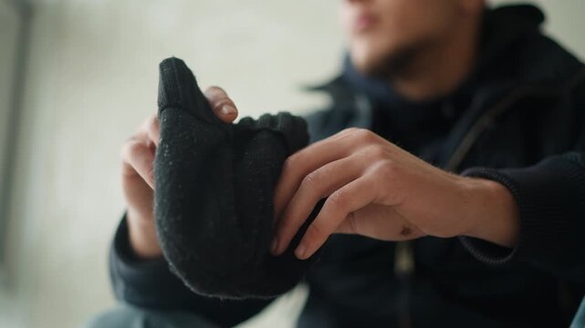 Close up of man holding and examining black knit fabric indoors. man manipulates material revealing its texture details against soft lighting in indoor setting with neutral background