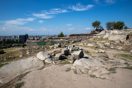 Plovdiv, Plovdiv Province, Bulgaria - 24 August 2018: View of the ancient ruins at Nebet Tepe with rocky terrain, scattered stones, and the city skyline under a blue sky.