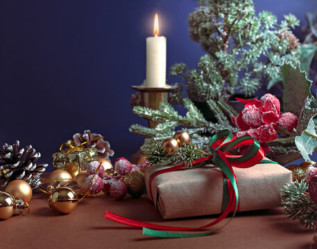 Christmas scene with handmade gift box with bow, candle, decorative fir branch, balls and cones for tree decoraton on blue wall background. New Year winter holiday composition with presents and decor.