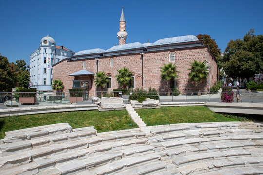 Plovdiv, Bulgaria - 24 August 2018: View of the historic Dzhumaya Mosque behind the ancient stone ruins of the Roman Stadium of Philippopolis under a clear blue sky.