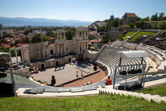Plovdiv, Bulgaria - 24 August 2018: View of the Ancient Theatre of Philippopolis with its stone seating and stage, set against the cityscape under a clear blue sky.
