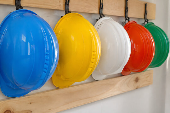 Several brightly colored hard hats are hanging on a wooden rack against a white background.