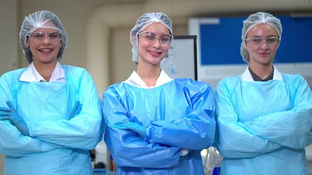 Portrait of three female laboratory researchers standing confidently together in protective clothing and safety goggles inside a modern scientific research laboratory.