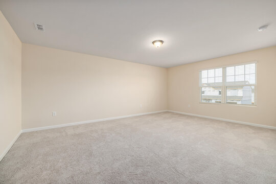 Empty room with neutral beige walls carpeted floor and a small window letting in natural daylight