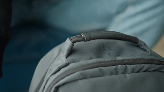 Close up of person hands gripping handle and adjusting items inside gray backpack. focus remains on texture details stitching lines zippers fabric material properties with soft lighting