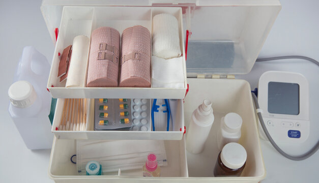 Top view of an organized first aid kit containing bandages, gauze, medical supplies, medicines, face masks, antiseptic spray, and a blood pressure monitor for healthcare, emergency care,