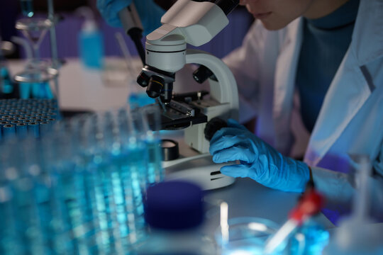 Scientist in lab coat and blue gloves performing medical research using a microscope, examining biological samples for biotechnology and pharmaceutical development