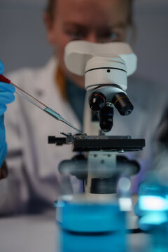 Scientist wearing blue gloves and lab coat preparing a sample on a microscope slide with a pipette, conducting research and chemical analysis in a modern laboratory