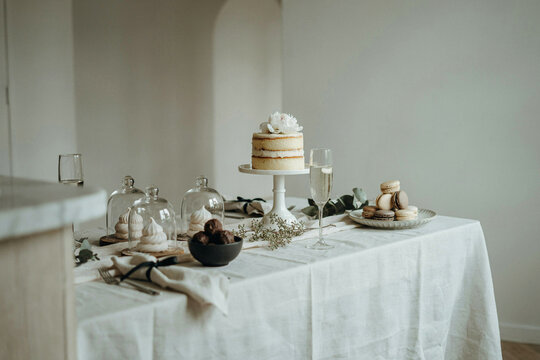 Elegant white frosted wedding cake on a table set with desserts and champagne glass