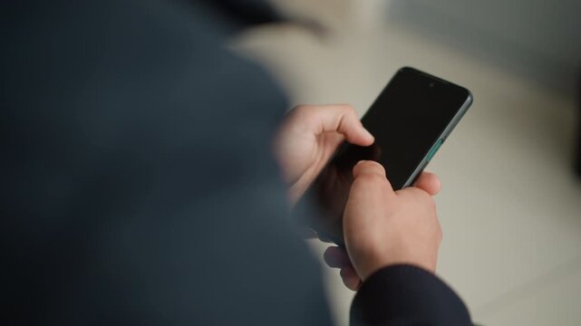 Close up of person holding and interacting with smartphone indoors. person hands are visible gripping device which remains off or inactive throughout. Soft lighting creates subtle shadows