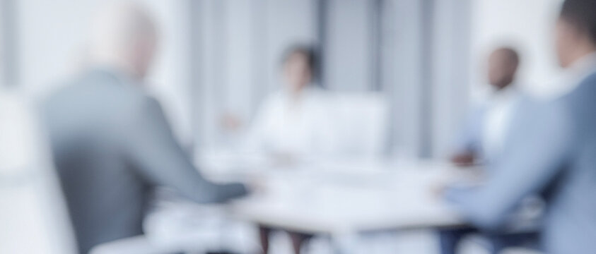 A professional meeting in a modern office setting, featuring blurred figures of diverse individuals engaged in discussion at a round table.
