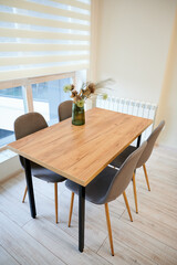 Fototapeta premium Wooden dining table with four chairs by window in bright modern apartment