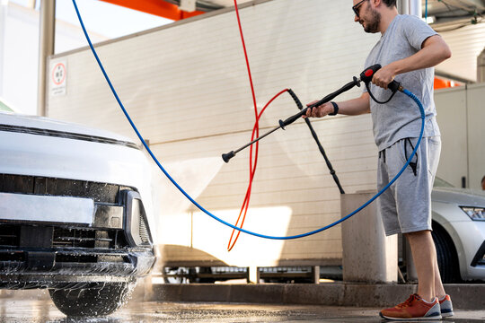 Man cleaning his car with a pressure washer, performing routine vehicle maintenance