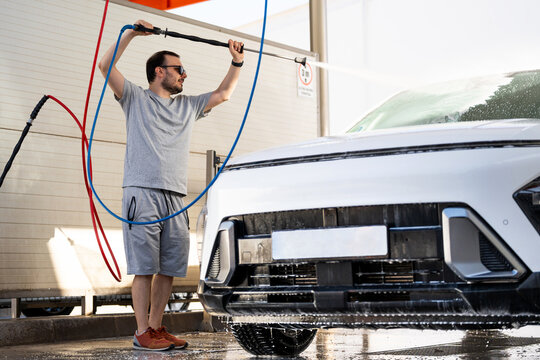 Young man washing car at self-service station using pressure washer for cleaning