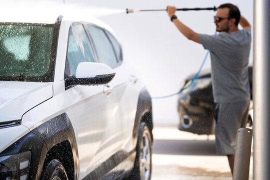 Young man washing car with pressure washer at a self-service car wash station