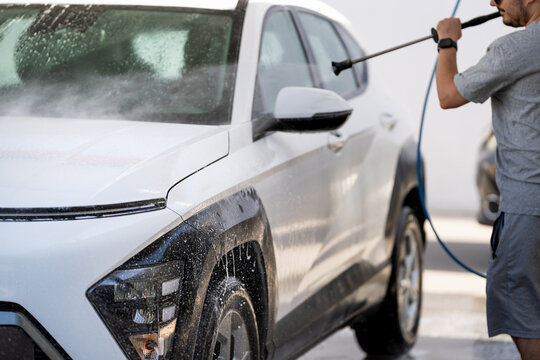 Man washing white suv with pressure washer at self service car wash station